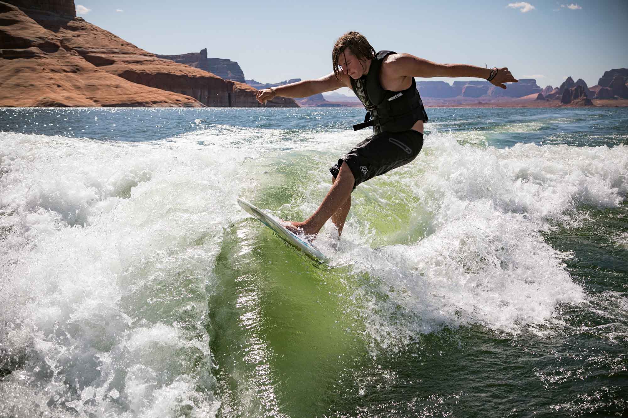 Crossroads residential treatment program student, participating in recreational therapy, wakeboarding a wave with red rock in the background.
